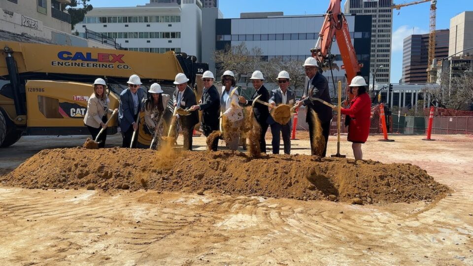 a group wearing hard hats uses shovels to move a pile of dirt