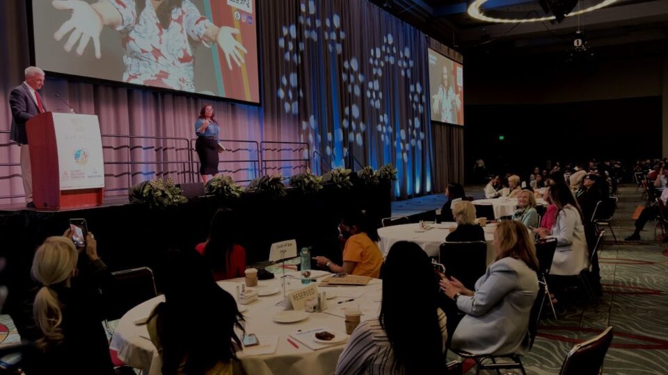 two people stand on stage at Live Well Advance