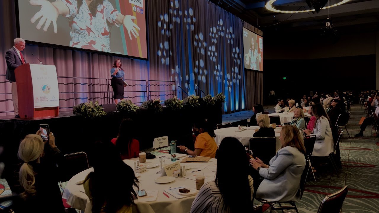 two people stand on stage at Live Well Advance