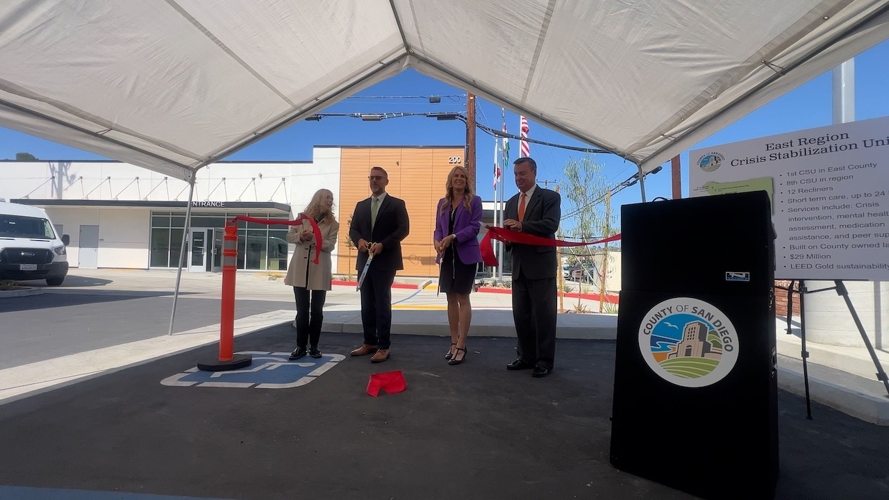 four people cut big red ribbon under tent