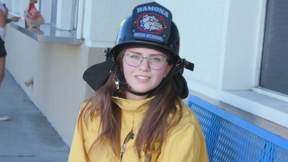 young person wearing firefighting helmet with "Ramona High School" on the front