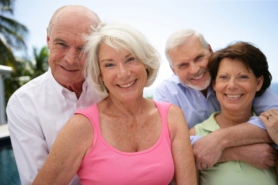 two older couples smile outside in front of tree