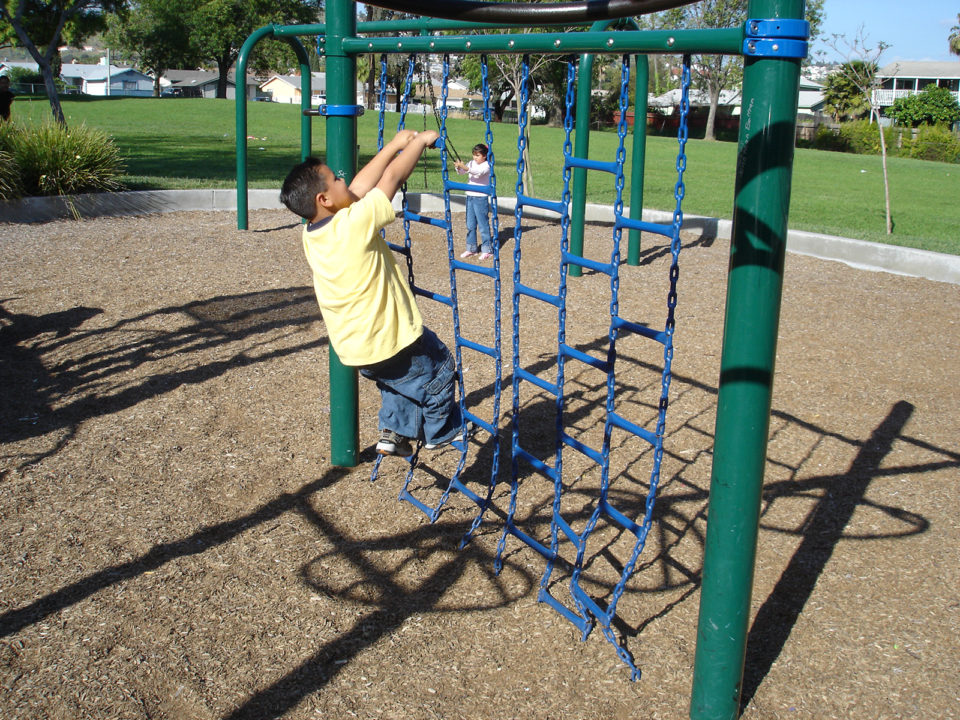 Child in yellow shirt and pants climbing a playground