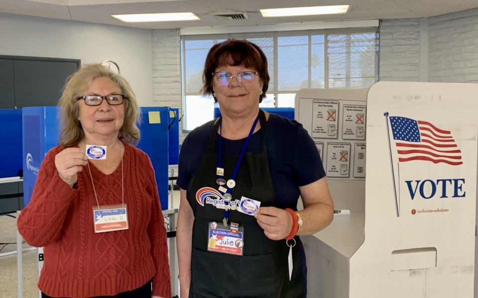 Smiling female bilingual poll workers holding up their badges.