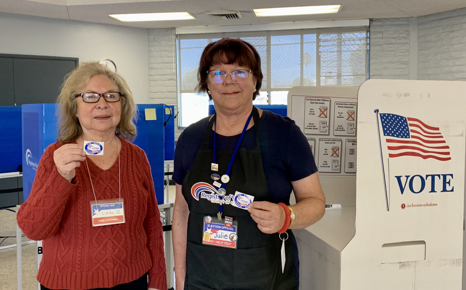 Smiling female bilingual poll workers holding up their badges.