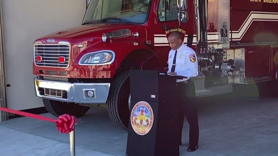 man stands at podium in front of fire engine