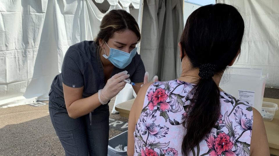 a masked woman gives a flu shot to another woman