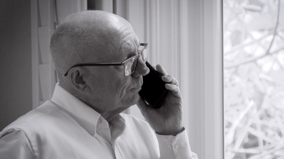 man holds cellphone up to ear while looking out window