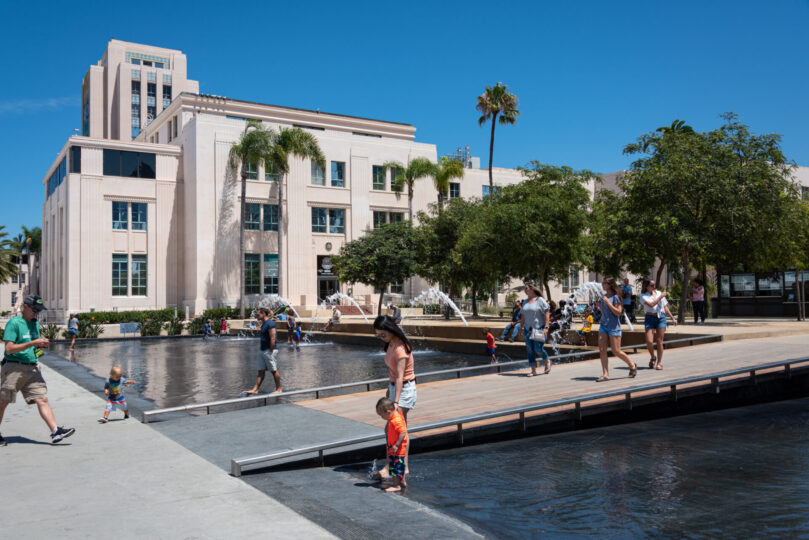 Photo of unidentified mother and son enjoying a warm summer day in the fountain at Waterfront Park in front of a County Administrative Building.