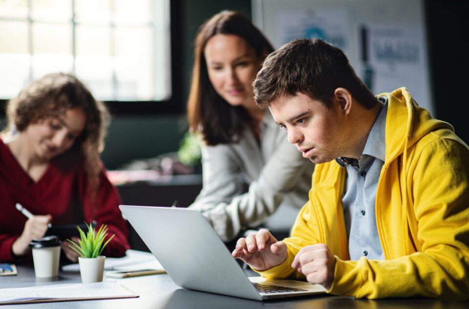 man typing on laptop with two people in the background