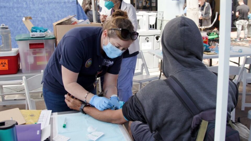 healthcare professional wearing mask treats person wearing hoodie
