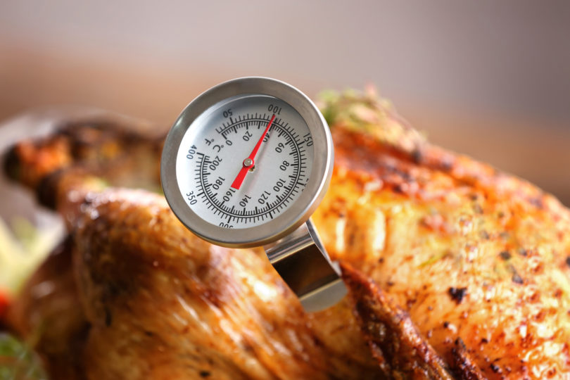 Roasted turkey with a food thermometer measuring internal temperature.