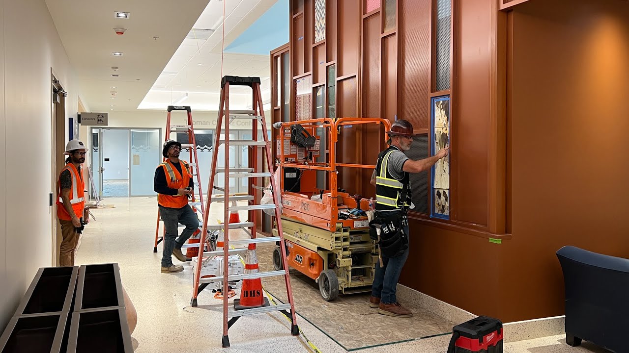 people with construction hats and vests work in an indoor space with ladders
