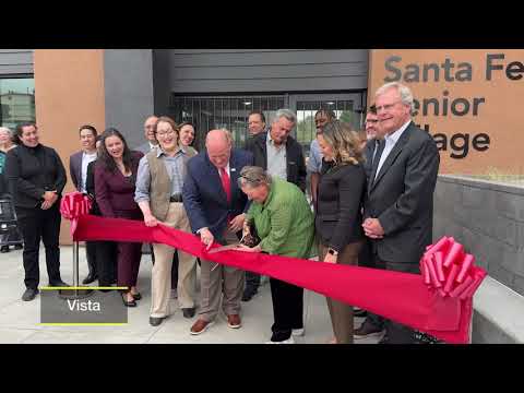 people cutting large red ribbon in front of building