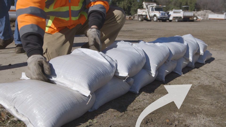 Person in an orange work vest placing sandbags in a row