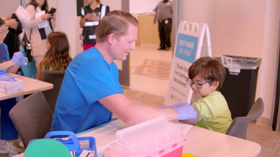 Child receiving flu vaccine from nurse wearing blur