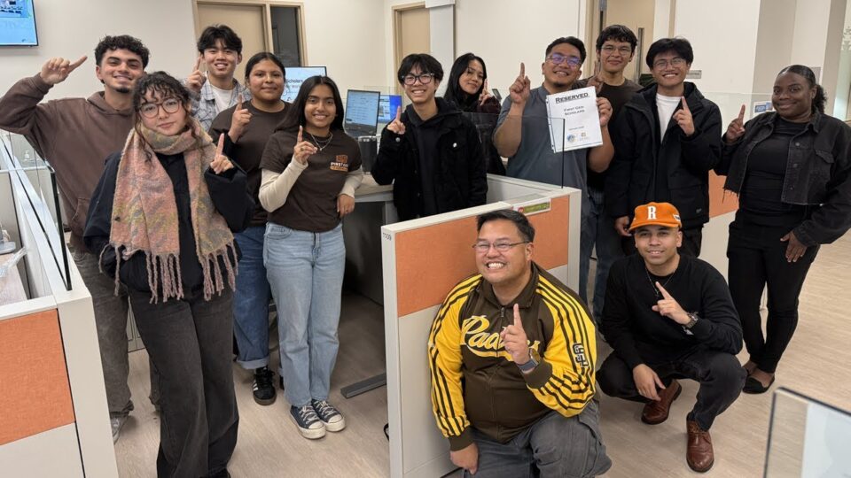 group gather around cubicle with one finger raised